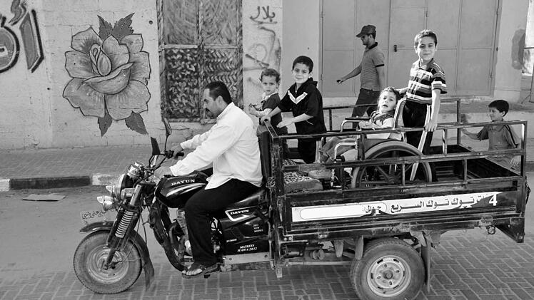Ein Vater transportiert seine Kinder, darunter einen Jungen im Rollstuhl, durch die Straßen irgendwo im Gaza. Foto: Till Mayer