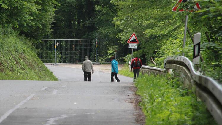 Neugierige inspizieren trotz des Verbots die gesperrte und abgesackte Straße in unmittelbarer Nähe des reißenden Mains