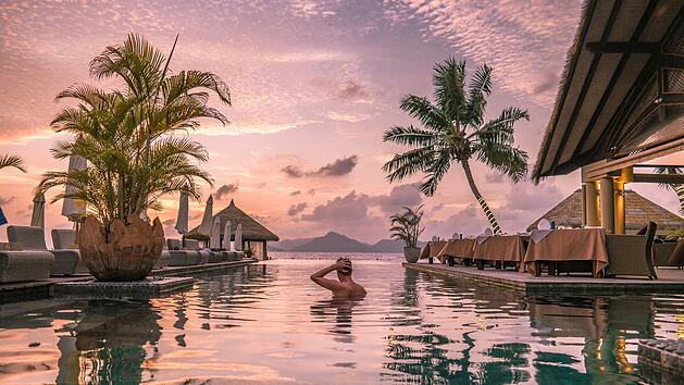 La Digue ist eine Insel der Seychellen im Indischen Ozean vor der Küste Ostafrikas. Sie ist für ihre Strände bekannt, wie den Anse Source d’Argent mit den Granitformationen an der Westküste. Junger Mann am Strand während seines Urlaubs auf den tropischen Seychellen, Männer im Infinity-Pool bei Sonnenuntergang auf der Seychellen-Insel La Digue  young man at the beach during vacation at the tropical islands of the Seychelles, men in infinity pool during sunset at the Seychelles La Digue Island  Summer vacation. Luxus-Urlaub - all inclusive