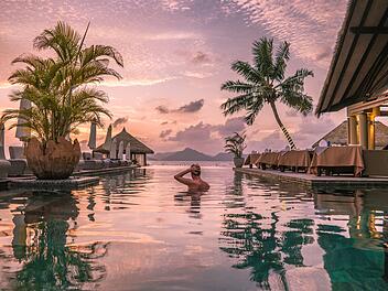 La Digue ist eine Insel der Seychellen im Indischen Ozean vor der Küste Ostafrikas. Sie ist für ihre Strände bekannt, wie den Anse Source d’Argent mit den Granitformationen an der Westküste. Junger Mann am Strand während seines Urlaubs auf den tropischen Seychellen, Männer im Infinity-Pool bei Sonnenuntergang auf der Seychellen-Insel La Digue  young man at the beach during vacation at the tropical islands of the Seychelles, men in infinity pool during sunset at the Seychelles La Digue Island  Summer vacation. Luxus-Urlaub - all inclusive