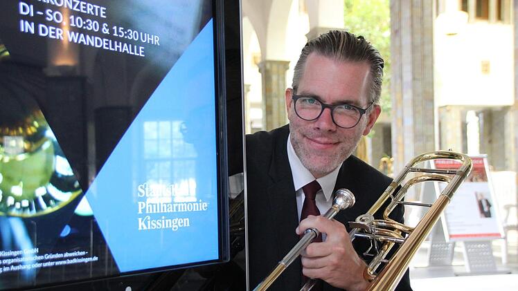 Posaunist Roman Riedel an einer Werbesäule, die auf den neuen Namen des Kurorchesters hinweist. Benedikt Borst