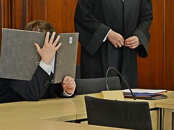 Der Angeklagte schützt sich im Gerichtssaal vor dem Blitzlichtgewitter der Fotografen. Foto: Pelke