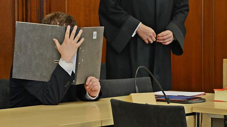 Der Angeklagte schützt sich im Gerichtssaal vor dem Blitzlichtgewitter der Fotografen. Foto: Pelke