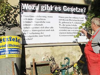 Der Trödelhändler, der das Geschäft seiner Frau betreibt, macht seinem Unmut über die Haltung des Jobcenters per Plakat Luft. Foto: Josef Hofbauer