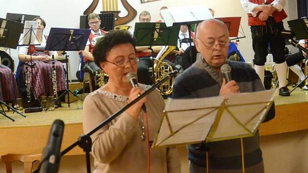 Brigitte B&uuml;ttner und Norbert Fehn und die "lustigen Musikanten" der Blaskapelle Buchbach (im Hintergrund) unter Leitung von Horst B&uuml;ttner er&ouml;ffneten das Wirtshaussingen in Buchbach.  Foto: Karl-Heinz Hofmann