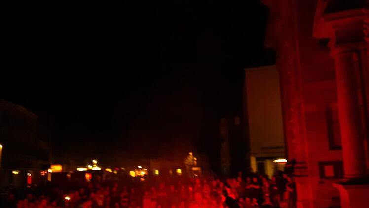Bei Nacht leuchtet rotes Licht eine Menschenmenge vor historischer Kulisse an. Die Atmosphäre wirkt mystisch, passend zu einem magischen Festival.