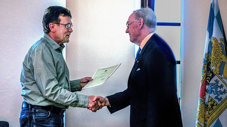 Die bayerische Fahne macht's feierlich: Josef Fuchs (links),  im Landratsamt Haßberge für Einbürgerungen zuständig, übergibt die  Einbürgerungsurkunde an Alan Stockbridge aus Ebern.Fotos: privat