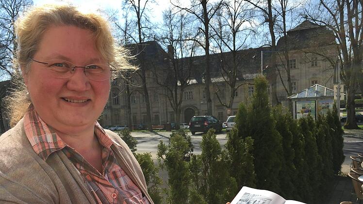 Ebrachs Archivarin Barbara Gülta mit einem Ebrach-Buch,  im Hintergrund die JustizvollzugsanstaltFoto: Anette Schreiber