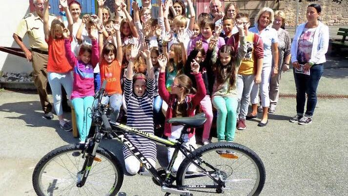 La Ola für ein neues Fahrrad. Im Bild (hinten, von links) Verkehrserzieher Hermann Dörfler, Anka Lubiato, Rosi Müller (Kiwanis), Verkehrserzieher Peter Schütz (verdeckt), Martin und Barbara Wohlfahrt, Bernt Pingel, Annegret Pachner, Doris Rötche (Kiwanis), Schulsekretärin Gisela Pingel und Rektorin Marion Hoffmann. Foto: Dieter Hübner