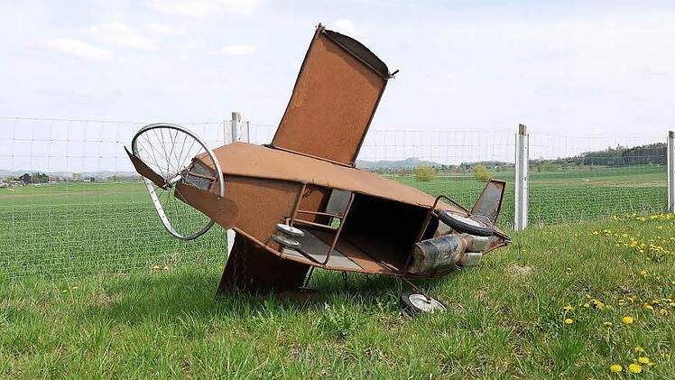 Ein Modell eines abgestürzten Flugzeugs, das von Gegnern des Flugplatzneubaus gebaut wurde, liegt auf einer Wiese nahe dem geplanten Standort für den neuen Verkehrslandeplatz. Foto: Berthold Köhler