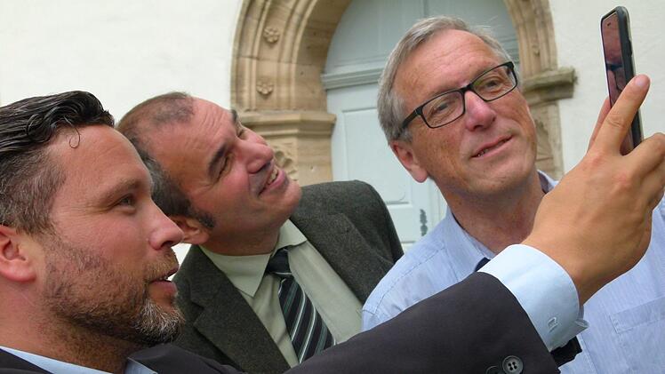 So funktioniert es: Mit dem Smartphone an der jeweiligen Station den Code eingeben und schon laufen hörbar und bildlich die Informationen, wie (von links) Martin Finzel, Rainer Maier und Rolf Gorny es vor der Ahorner Kirche demonstrieren. Foto: Lothar Weidner