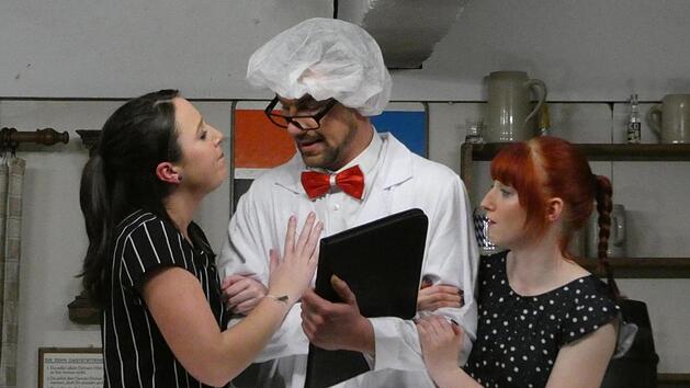 Die Tochter des Wirts (links, Jessica Ebert) und die Bedienung (rechts, Lisa Stengel) bezirzen Gesundheitsinspektor Dr. Riesling alias Sebastian Kreb, um eine wohlwollende Bewertung der Gastwirtschaft zu erreichen.  Fotos: Christian Licha