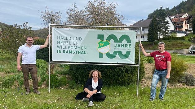 Die Vorsitzenden des SV Ramsthal Jan Gawlik (von links), Anja Langbroek und Udo Schaub vor einem Plakat, das auf das Jubiläum hinweist.