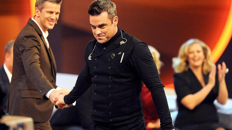US-S&auml;nger Robbie Williams verabschiedet sich am 03.11.2012 in der ZDF-Show &laquo;Wetten, dass..?&raquo; in der &Ouml;VB-Arena in Bremen von Moderator Markus Lanz (l) w&auml;hrend die Wettpatin und Schauspielerin Barbara Sch&ouml;nberger dahinter klatscht. Foto: Ingo Wagner/dpa