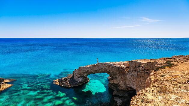 Wird die Love Bridge ihrem Hype gerecht? - Frau auf dem wundersch&ouml;nen nat&uuml;rlichen Felsbogen in der N&auml;he von Ayia Napa, Cavo Greco und Protaras auf der Insel Zypern im Mittelmeer. Legend&auml;re Br&uuml;ckenliebhaber. Atemberaubendes blaugr&uuml;nes Meer und sonniger Tag. Woman on the beautiful natural rock arch near of Ayia Napa, Cavo Greco and Protaras on Cyprus island, Mediterranean Sea. Legendary bridge lovers. Amazing blue green sea and sunny day.