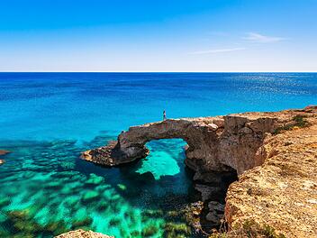 Wird die Love Bridge ihrem Hype gerecht? - Frau auf dem wundersch&ouml;nen nat&uuml;rlichen Felsbogen in der N&auml;he von Ayia Napa, Cavo Greco und Protaras auf der Insel Zypern im Mittelmeer. Legend&auml;re Br&uuml;ckenliebhaber. Atemberaubendes blaugr&uuml;nes Meer und sonniger Tag. Woman on the beautiful natural rock arch near of Ayia Napa, Cavo Greco and Protaras on Cyprus island, Mediterranean Sea. Legendary bridge lovers. Amazing blue green sea and sunny day.