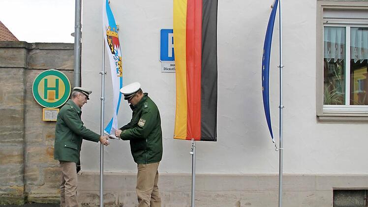 Die Polizisten Peter Wolf und Ralph Hanschkow (von links) hissen die bayerische Staatsflagge, die deutsche und die europäische Fahne vor der Bad Staffelsteiner Polizeistation auf Halbmast. Foto: Thomas Heuchling