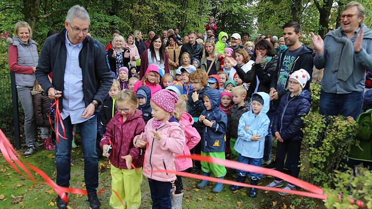 Bürgermeister Bernd Drummer durchschneidet mit Lisa und Amelie das Band. Die restliche Kinderschar kann es kaum erwarten, dass der neue Spielplatz endlich freigegeben wird. Foto: Franz Galster