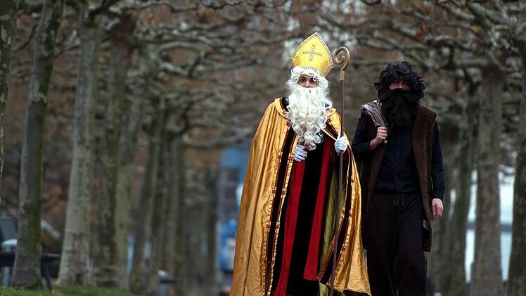 Mitglieder vom Bund der Deutschen Katholischen Jugend gehen als Nikolaus (l) und Knecht Ruprecht verkleidet am Rheinufer entlang. Eine Gr&uuml;nen-Politikerin aus Nordrhein-Westfalen h&auml;lt den strengen Gehilfen des Nikolaus f&uuml;r &uuml;berholt. Foto: Federico Gambarini/dpa