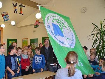 Erneut darf sich die Grundschule Umweltschule in Europa nennen. Hier sind die Kinder und Schulleiter Roland Schmidt mit Begeisterung dabei, die neue grüne Fahne im Schulhaus Lauter zu hissen. Foto: Kathrin Kupka-Hahn