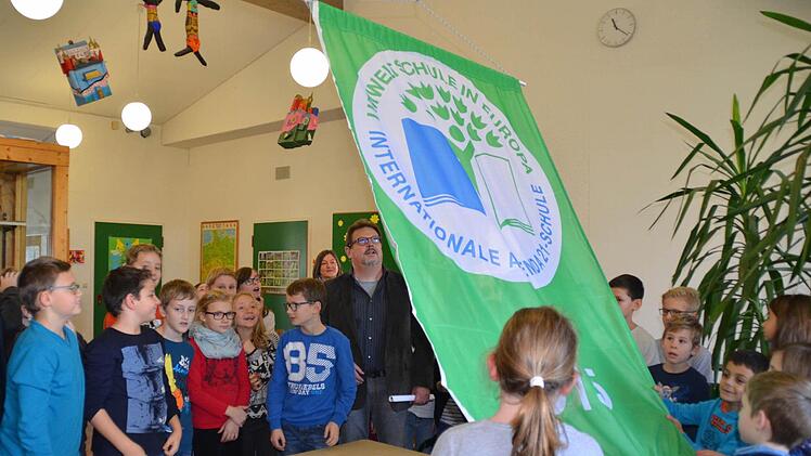 Erneut darf sich die Grundschule Umweltschule in Europa nennen. Hier sind die Kinder und Schulleiter Roland Schmidt mit Begeisterung dabei, die neue grüne Fahne im Schulhaus Lauter zu hissen. Foto: Kathrin Kupka-Hahn