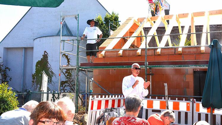 Der Vorsitzende des Diakonievereins Maroldsweisach, Pfarrer Wolfgang Scheidel, heißt zum Richtfest willkommen. Im Hintergrund die katholische Herz-Jesu-Kirche. Auf dem Dachstuhl wartet bereits Dieter Hepp, um seinen Richtspruch zu halten.  Foto: Gerhardt Schmidt