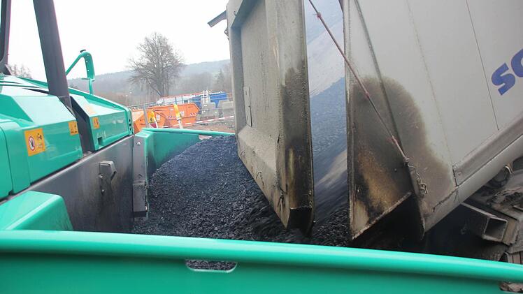 Der heiße Asphalt ergießt sich aus dem Laster in die Asphaltmaschine. Foto: Friedwald Schedel
