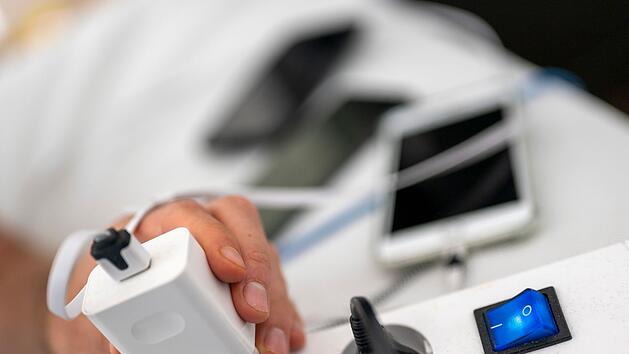 Ein Mann zieht den Stecker eines Ladegeräts für ein Smartphone aus einer Steckdosenleiste.