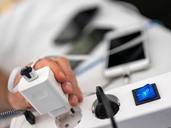 Ein Mann zieht den Stecker eines Ladegeräts für ein Smartphone aus einer Steckdosenleiste.