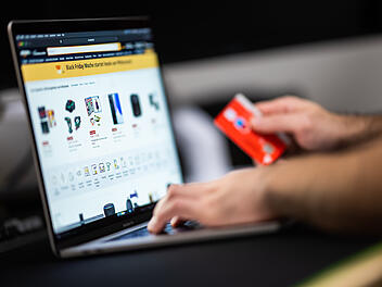 Ein Mann mit einer Bankkarte in der Hand sitzt am Laptop und schaut sich die Black Friday Angebote auf der Online-Shopping-Seite von Amazon an.