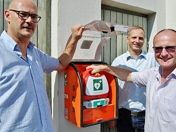 ZTM-Projektmanager Thomas Schreiner (Mitte) montierte im Beisein der beiden Stadträte Klaus Zehe (links) und Walter Schuhmann den Automatisierten Externen Defibrillator (AED) am Feuerwehrhaus in Albertshausen. Foto: Sigismund von Dobschütz
