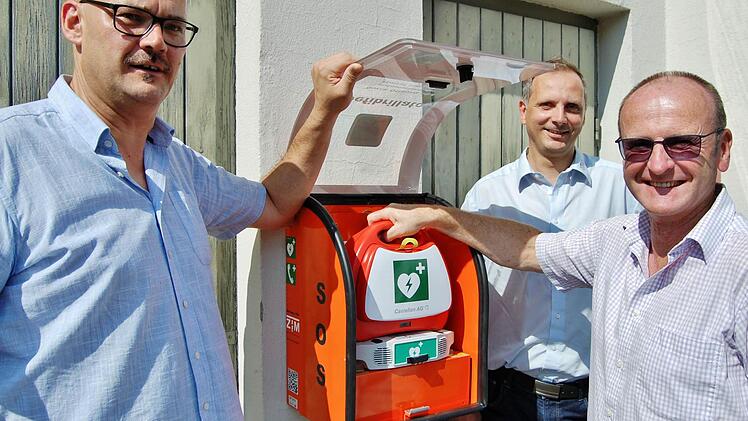 ZTM-Projektmanager Thomas Schreiner (Mitte) montierte im Beisein der beiden Stadträte Klaus Zehe (links) und Walter Schuhmann den Automatisierten Externen Defibrillator (AED) am Feuerwehrhaus in Albertshausen. Foto: Sigismund von Dobschütz