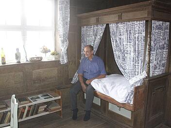Artur Fischer sitzt auf dem Himmelbett, in dem 1632 der Feldherr Wallenstein übernachtete, als er mit seinen Soldaten durch den Itzgrund zog. Das Wallenstein-Zimmer befindet sich in Fischers historischem Anwesen in der Gleußener Ortsmitte. Foto: Matthias Einwag