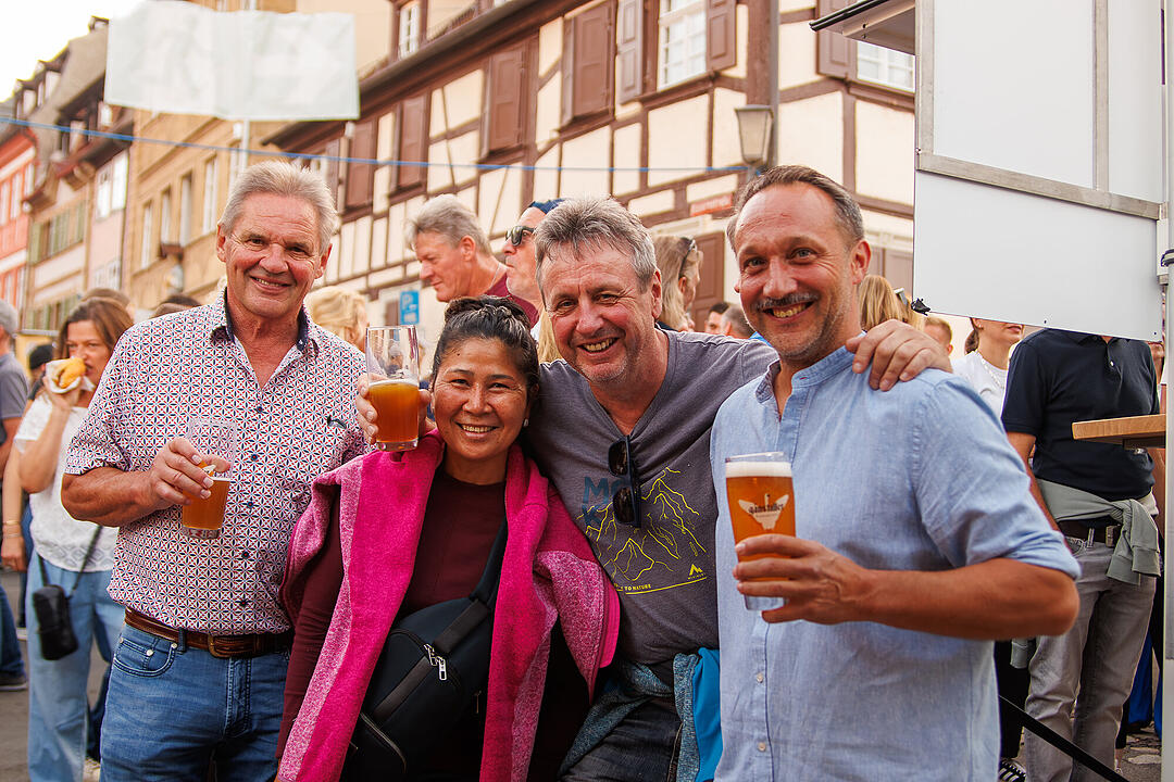 Menschen feiern auf der Bamberger Sandkerwa, l&auml;chelnd mit Biergl&auml;sern in der Hand, umgeben von Fachwerkgeb&auml;uden.