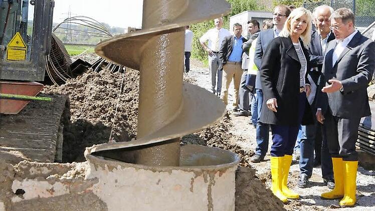 Ein riesiger Bohrer gräbt Löcher an den Stellen in den Untergrund, an denen später Spundwände elf Meter tief in den Boden getrieben werden. Unser Bild zeigt Umweltministerin Ulrike Scharf bei der Baustellen-Besichtigung im Gespräch mit OB Henry Schramm. Fotos: Matthias Hoch
