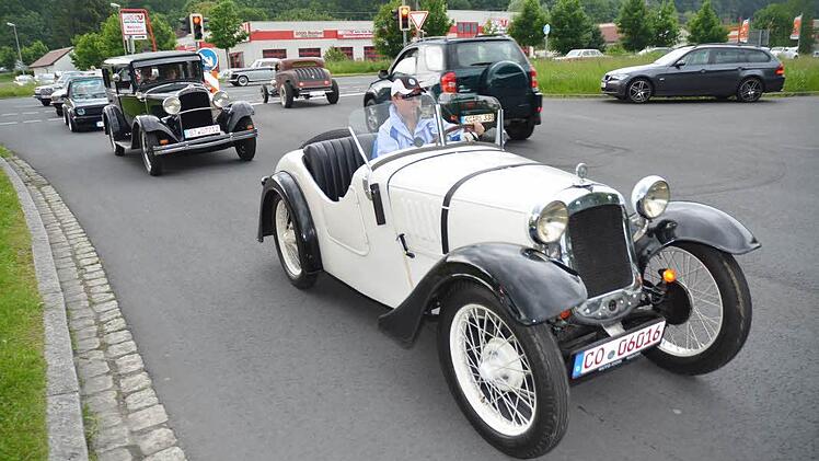 Rassige Karossen bei der Ausfahrt: vorne ein BMW Dixi (weiß, Baujahr 1926), dahinter ein Dodge (Baujahr 1928), rechts hinten an der Ampelanlage ein Chevrolet Hot Rod.