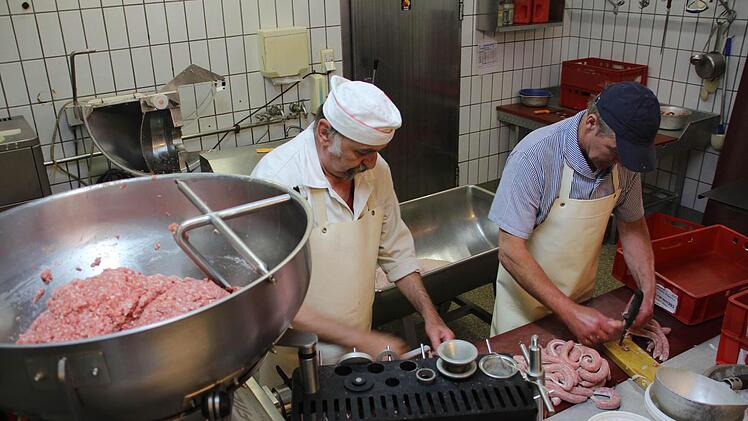 Seit über 40 Jahren arbeitet Paul Sponsel (links) im Betrieb. Er füllt die Würste, während Peter Wehrfritz die Wurstkette zerteilt.  Foto: Sarah Dann