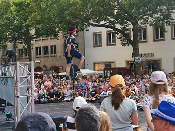 Ein Jongleur auf Stelzen unterh&auml;lt ein gro&szlig;es Publikum bei "Bamberg zaubert". Die Menge staunt begeistert im Freien, w&auml;hrend die B&auml;ume Schatten spenden. Rundum ist Festivalatmosph&auml;re sp&uuml;rbar.