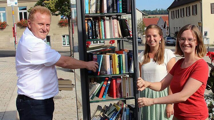 Dieser Bücherschrank steht auf dem Maßbacher Marktplatz. Jeder darf Bücher entnehmen und hineinstellen. Zur Inbetriebnahme kamen Bürgermeister Matthias Klement (links, Allianzmanagerin Hannah-Rabea Grübl (rechts) und ihrer Praktikantin Miriam Mai.  Foto: Dieter Britz