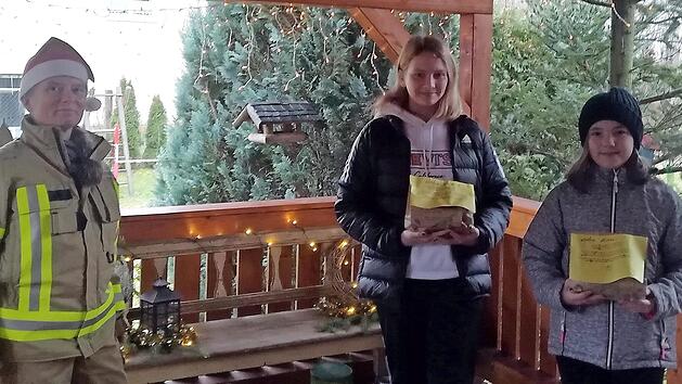 Die Jugend- und Kinderfeuerwehr Dörfles bemalte Stern-Weihnachtskarten mit winterlichen Motiven. Die Leiterin der "Feuerwehrbande" Dörfles, Geli Kempf (linkes Foto, l.), beschenkt Zoe und Kimara Höfner, aktive Mitglieder der Jugend- und Kinderfeuerwehr Dörfles. Die bunten Weihnachtsgrüße sind auf dem rechten Foto zu sehen. Fotos: privat