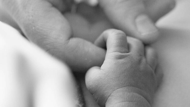 Abschied vom Sternenkind: Eine Erwachsenenhand berührt kleine, leblose Finger. Vom Aussehen her erinnert das Bild an ein Foto aus einem normalen Baby-Shooting.  Foto: Kai Gebel/Dein-Sternenkind