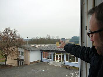 Da ist das Ding: Bürgermeister Markus Mönch zeigt auf das Turnhallendach, durch das die Wärme mehr oder weniger ohne bremsende Isolation hinaus in die Landschaft pfeift. Foto: Berthold Köhler