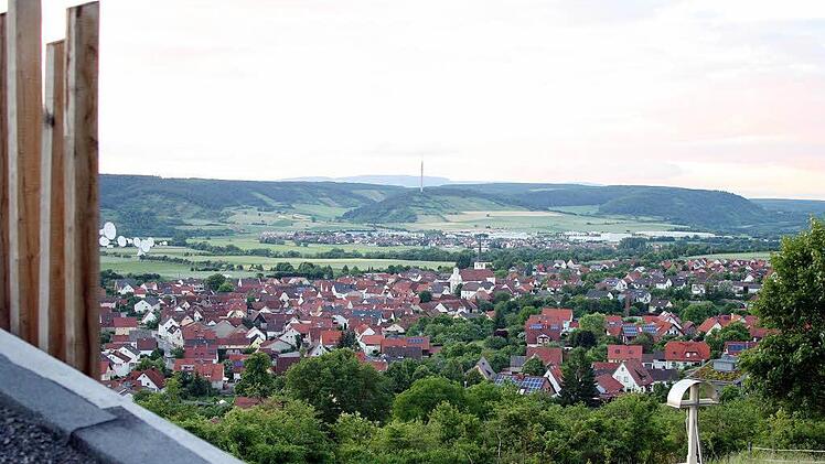 Blick vom Dach der Dreifaltigkeitskapelle aus über die Stelen und das Flurkreuz am Heinig auf die Ortschaft Fuchsstadt und das idyllische Saaletal.