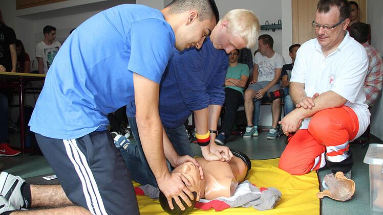 Ahmet Bozhügük und Michael Frank üben die Herz-Lungen-Wiederbelebung an einer Simulationspuppe. Frank Schmidt vom Coburger BRK leitet sie dabei an (von links). Foto: Helke Renner