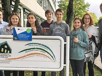 Die Projektleiter Erik H&uuml;neburg (rechts) und Tillmann Leibing (links) pr&auml;sentieren mit teilnehmenden Sch&uuml;lern das offizielle Schild, das k&uuml;nftig am Eingang des Ernestinums auf das europ&auml;ische Kooperationsprojekt hinweisen wird.  Foto: Bernd Jakob