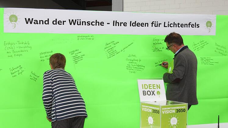 Auf leuchtendem Grün bringen zwei Besucher der Zukunftswerkstatt ihre Anregungen an.