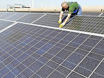 Auf dem Symbolbild arbeiten Mitarbeiter einer Umweltfirma an Photovoltaik-Paneln, die auf einem Dach angebracht sind. Foto: Holger Hollemann dpa/lni