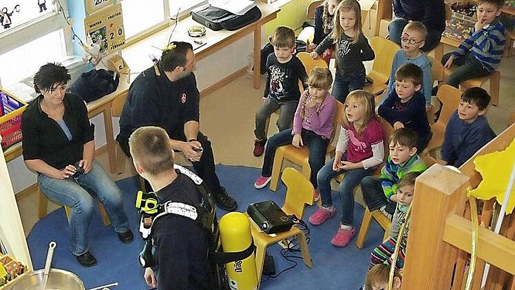 Dominik Fischer führt den Jungen und Mädchen seine Feuerwehrausrüstung vor. Mit im Bild sind (sitzend von links) Kindergarten-Leiterin Johanna Höfner und Kommandant Frank Fischer.  Foto: Heike Schülein