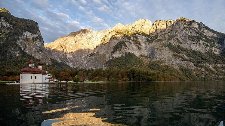 Die Kapelle Sankt Bartolomä am Königssee vor dem Watzmann, der von der Morgensonne angestrahlt wird und sich im Wasser spiegelt.