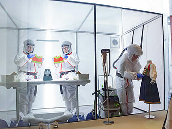 Spezialisten in Schutzanzügen reinigen historische Kleidung in Nürnberger Museum